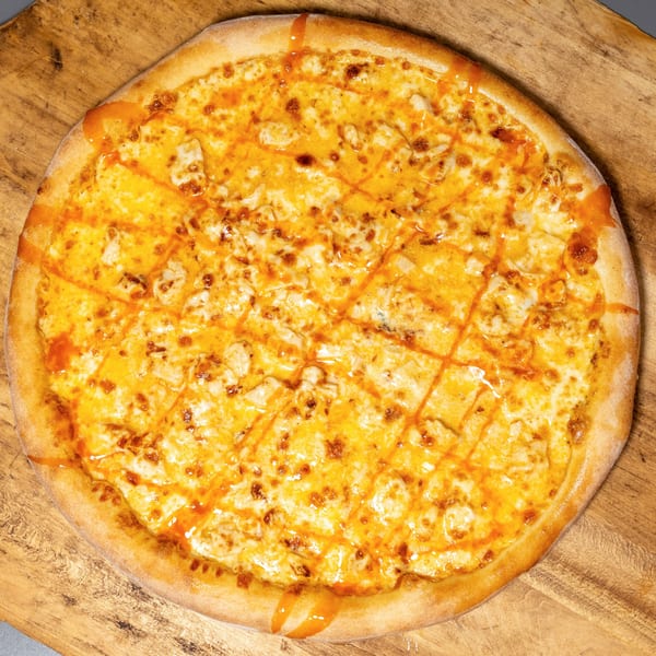 Uncle Vito's Pizzeria's Buffalo Chicken Pizza, topped with cheese and buffalo sauce drizzle, on a wooden board.