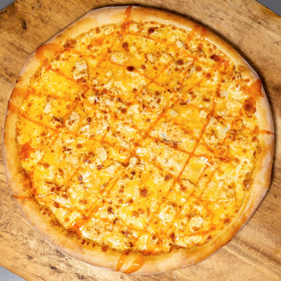 Uncle Vito's Pizzeria's Buffalo Chicken Pizza, topped with cheese and buffalo sauce drizzle, on a wooden board.