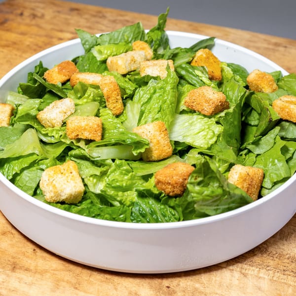 A white bowl filled with fresh green romaine lettuce and golden croutons on a wooden surface.