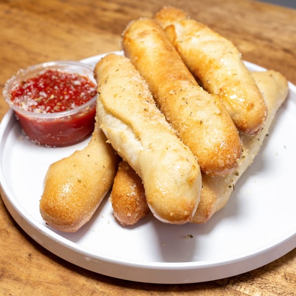 Golden-brown garlic breadsticks with herbs and parmesan, served with a side of marinara sauce.
