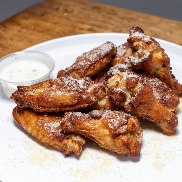 Crispy, golden-brown chicken wings dusted with Parmesan cheese, served with a side of ranch dressing.
